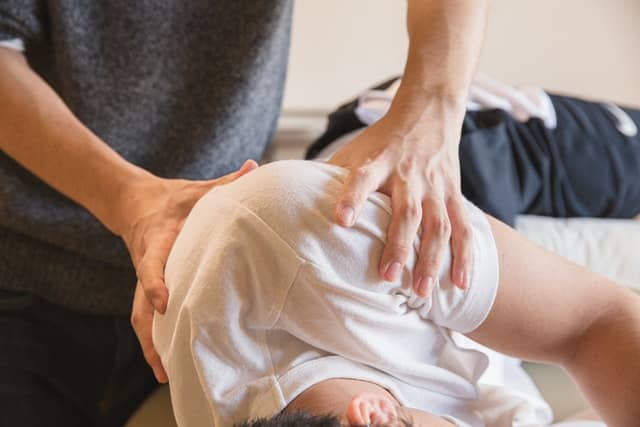 A physical therapist grips the shoulder of a patient